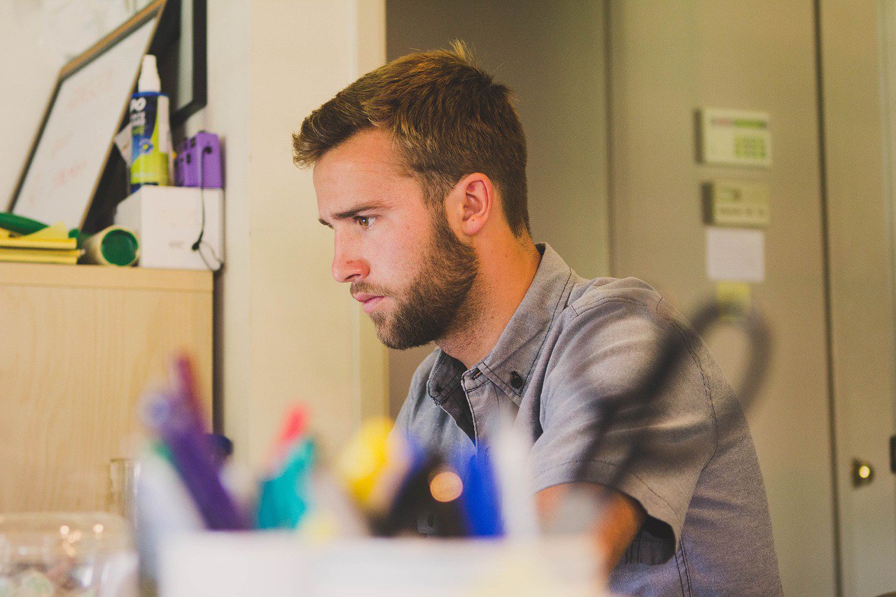 Man concentrating at desk with office supplies and shelves in background.