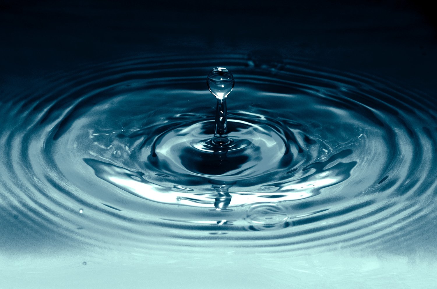 Close-up photo of a water droplet causing ripples on a water surface, with a central splash.