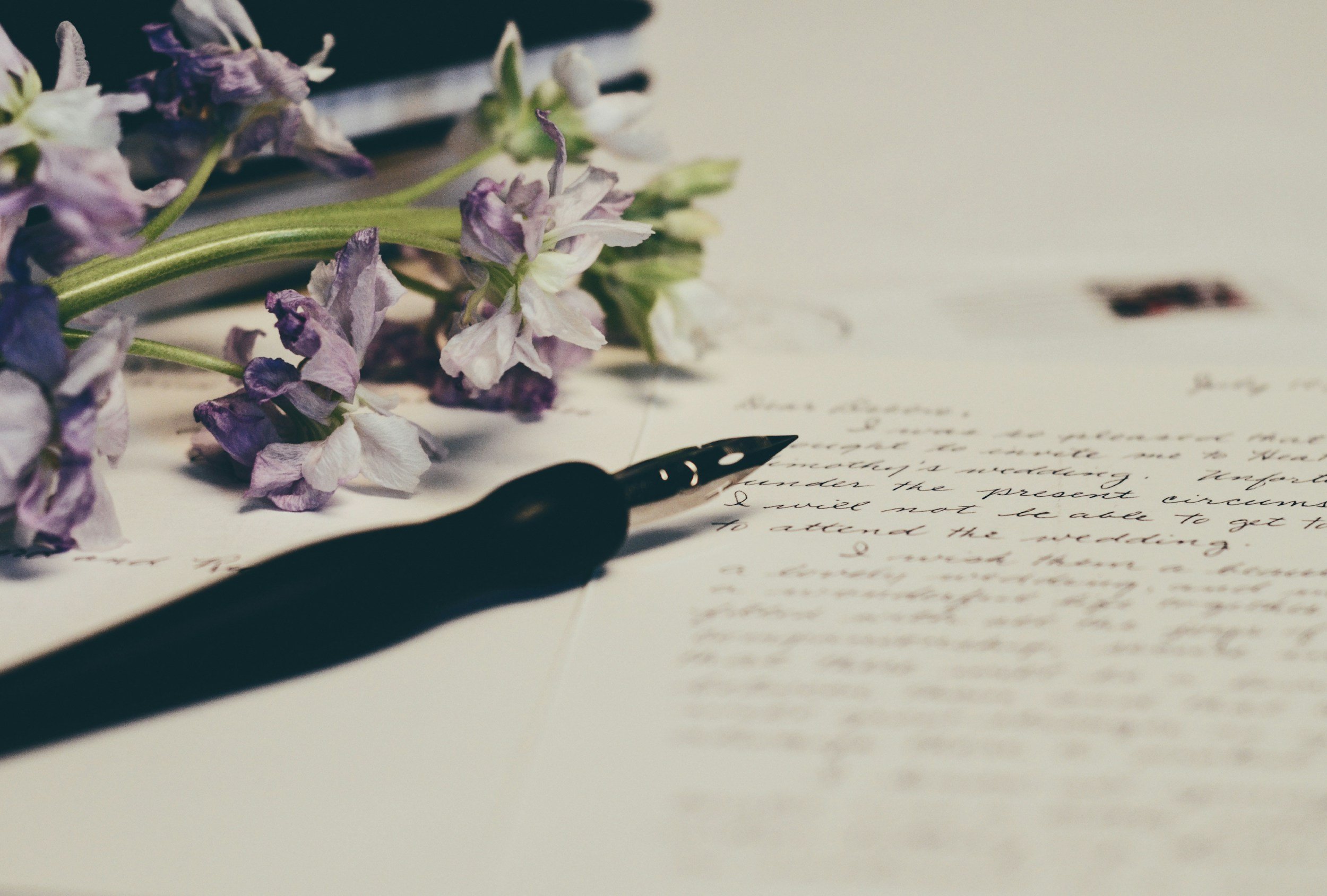 A pen rests beside a bouquet of flowers on a desk, with a handwritten will partially visible in the background.