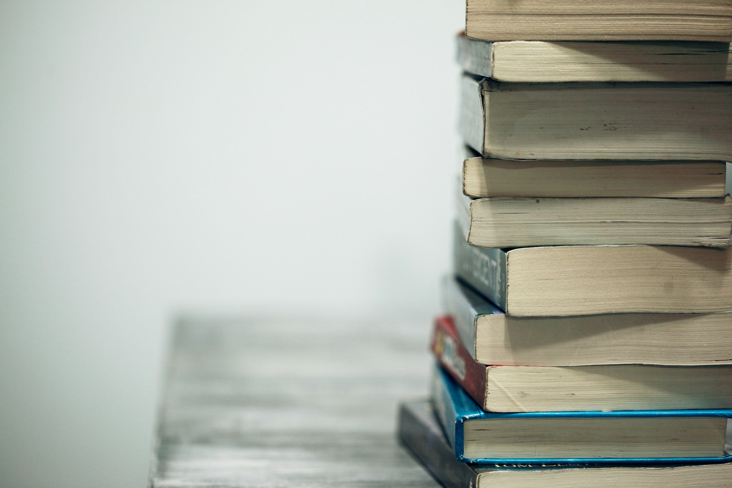 A neatly arranged stack of books resting on a wooden table, showcasing various colors and sizes.