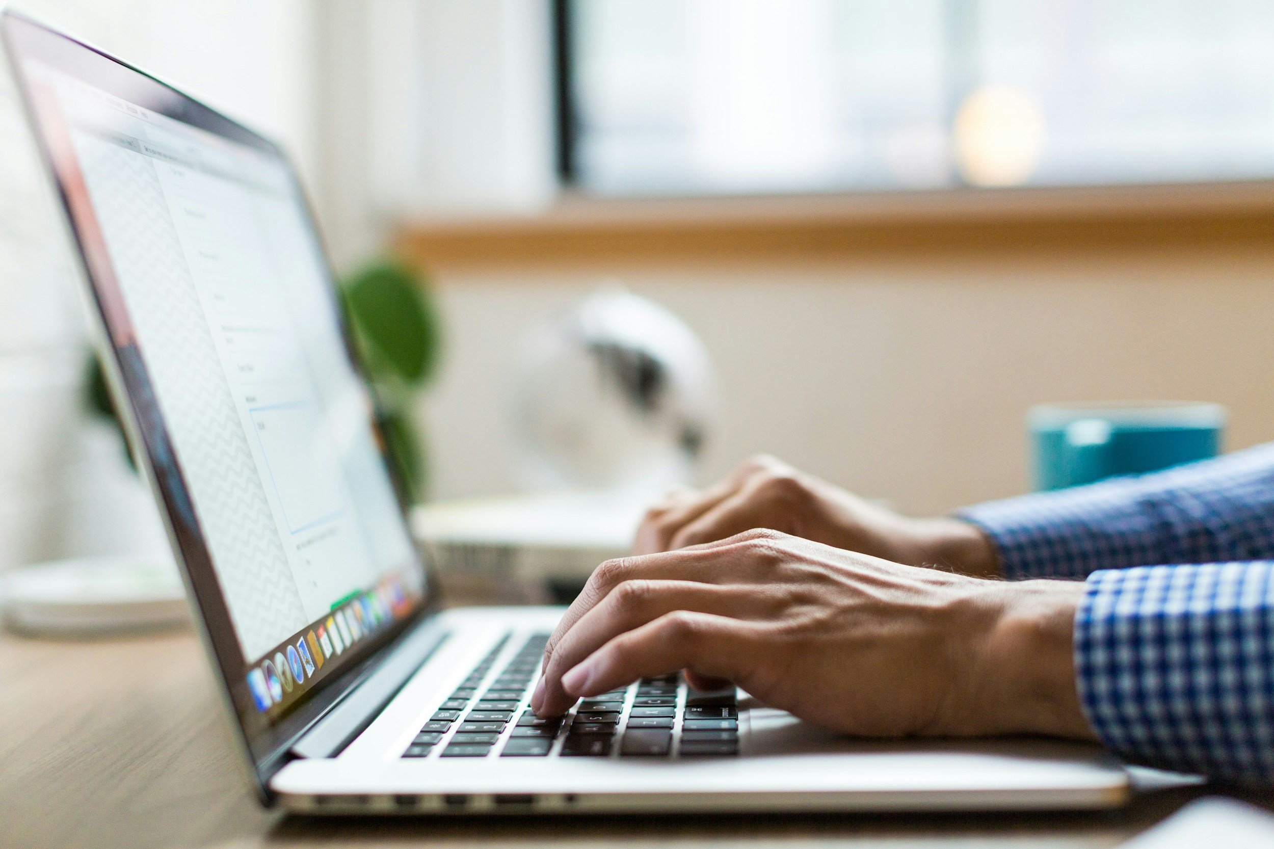 A man in a smart shirt typing on his laptop.