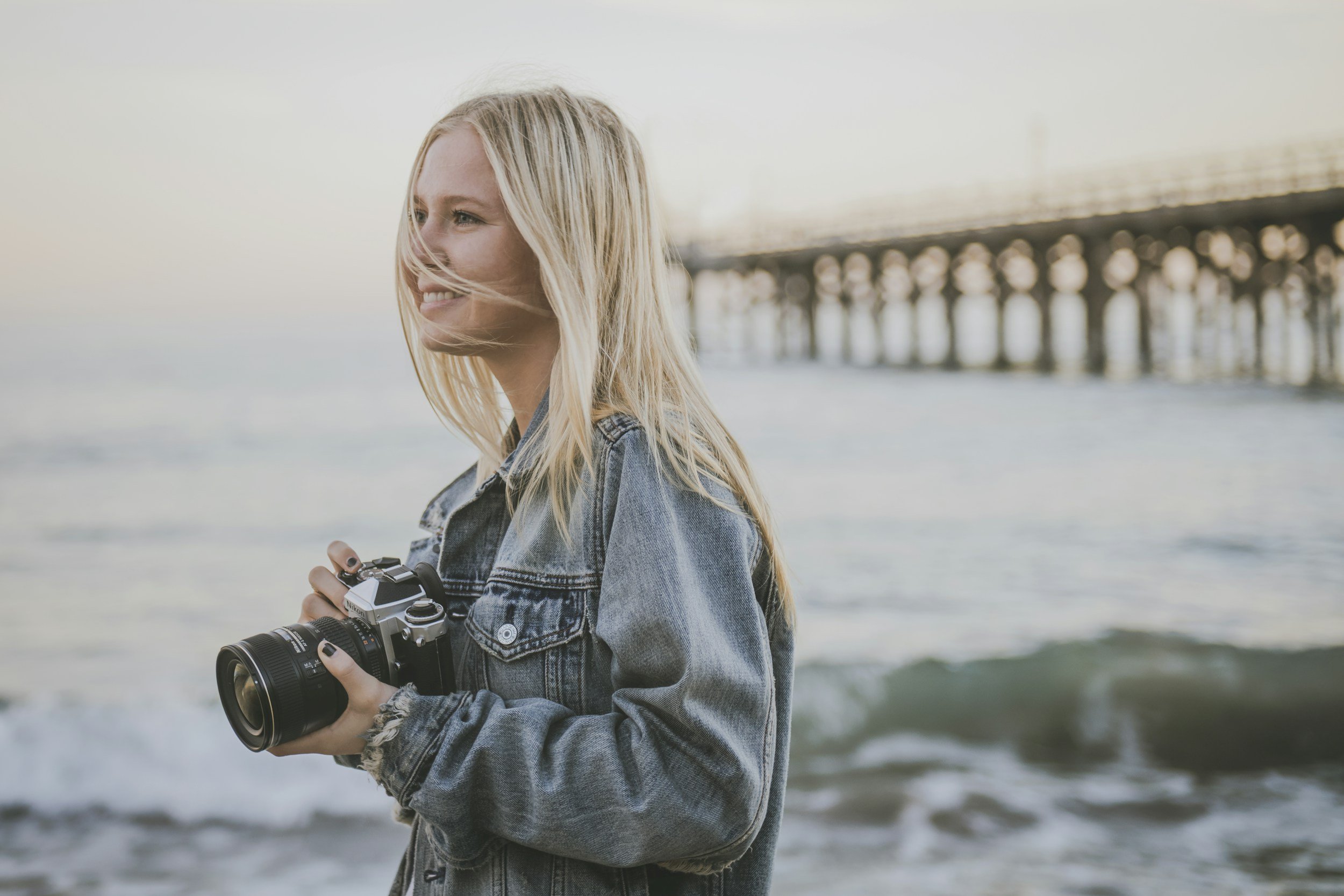 A female photographer standing on a beach with waves in the background.
